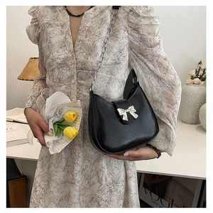 Close-up of the black leather baguette bag featuring a silver metal bow buckle detail