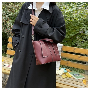 Macro detail of wine red leather bucket bag with metallic rivets and shoulder strap
