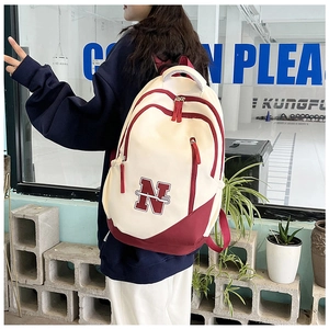 Detail showing contrasting cream and burgundy colors with stitched letter N on the backpack