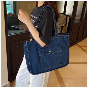 Detail of spacious dark blue denim tote bag with metal button pocket worn by model