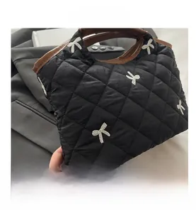 Close-up of black quilted handbag featuring white embroidered bows and leather handles