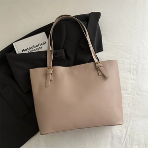 Detail of minimalist beige tote bag with gold metal buckle on a dark grey blazer background