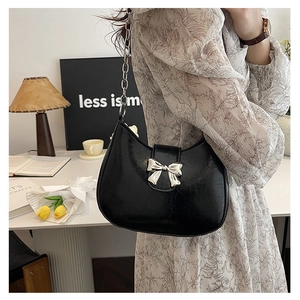 Detail of black pleated shoulder bag with silver metal bow clasp and chain strap