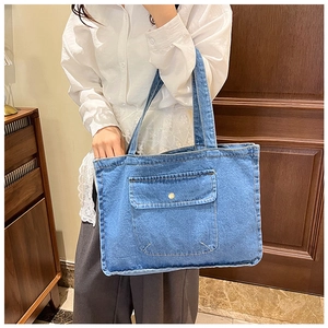 Blue denim tote bag with visible stitching and gold button detail worn by a model