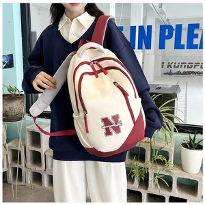 Detail of college style backpack featuring cream canvas and burgundy trim with N embroidery