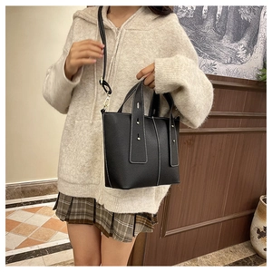 Detail of black pebbled leather bucket bag with white contrast stitching and shoulder strap