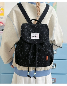 Detail showing black corduroy backpack with bow patterns and branded woven label