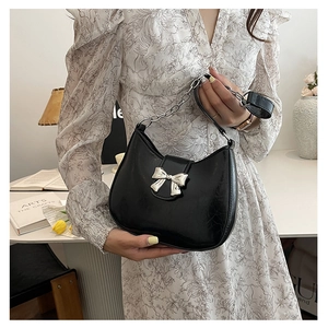 Detail of black leather half-moon shoulder bag with silver bow charm and chain handle