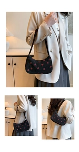 Close-up of black corduroy fabric featuring detailed red strawberry embroidery on underarm bag