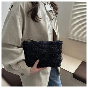 Detail of elegant black clutch bag featuring 3D rose textures and ruffled lace design