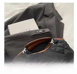Detail of black quilted handbag featuring white bow embroidery and brown leather handle