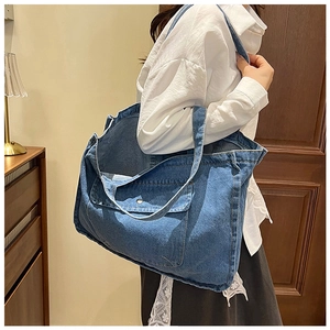 Close-up of a blue denim tote bag with functional flap pocket and metal button detail