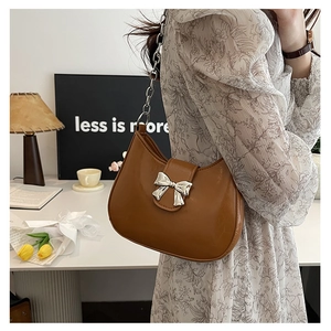 Close-up of brown leather shoulder bag with silver bow accent and metal chain strap