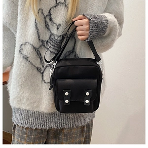 Detail of black canvas crossbody bag with four white decorative buttons on the front pocket