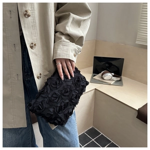 Close-up of black 3D rose textured evening clutch bag held by a model in casual attire