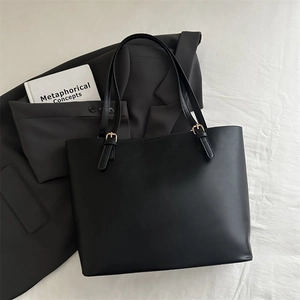 Detail view of black leather tote bag with adjustable shoulder straps and gold metal buckles