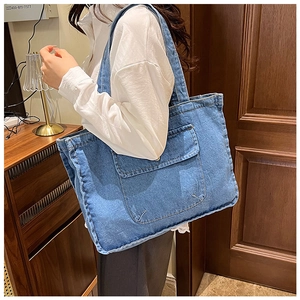 Detail shot of a dark blue washed denim tote bag with a front pocket and button detail