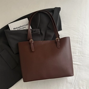 Detail view of large brown tote bag with matte leather and golden metal hardware