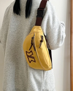 Detail view of mustard yellow nylon chest bag with adjustable brown strap on a model