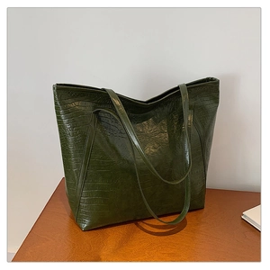 Close-up of deep green crocodile embossed tote bag with glossy finish on wooden surface