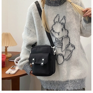 Detail view of black canvas crossbody bag with white buttons and adjustable strap