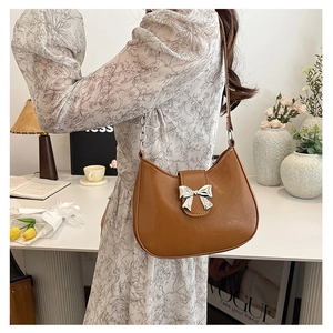 Close-up of caramel brown underarm bag featuring glossy leather and a silver bow buckle