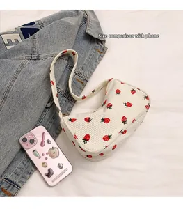 Size comparison of white corduroy underarm bag with strawberry print next to a phone