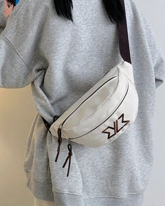 Close-up of white crescent crossbody bag with brown embroidered logo and adjustable strap