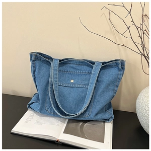Detailed close-up of blue denim tote bag with gold metal snap button and front pocket