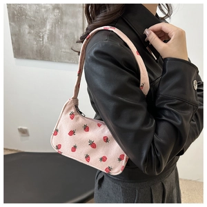 Sac sous le bras en velours rose à motif fraise porté par un mannequin stylé