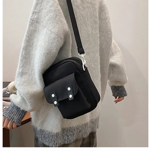 Detail of black canvas crossbody bag with decorative white buttons on grey sweater