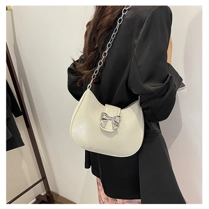 Detail of a creamy white moon bag with a silver metal bow and shiny chain strap