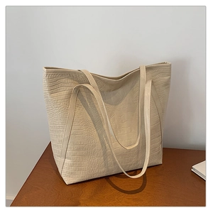 Detail of the cream-white tote bag with embossed crocodile texture on a wooden surface