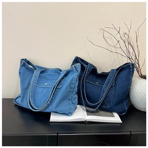 Detail of light and dark blue denim tote bags with outer pockets and metal buttons