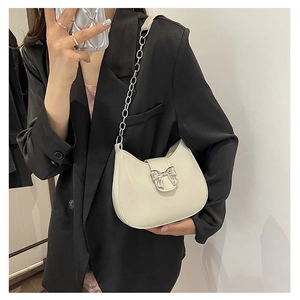 Detail shot of white shoulder bag with silver bow buckle and chain strap on a model