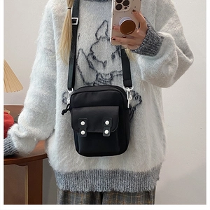 Detail view of black nylon crossbody bag featuring double white decorative buttons