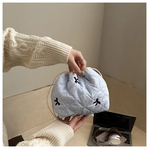 Detail of light blue quilted drawstring bucket bag with black bow embroidery and fabric texture