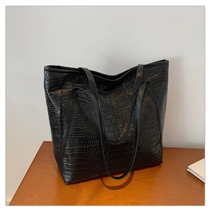 Detail of black faux leather tote bag with crocodile pattern on a wooden table