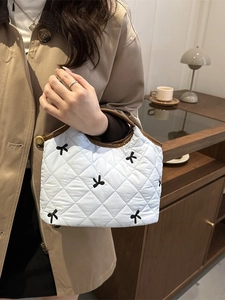 Quilted white handbag with bow embroidery and brown handles held by a model