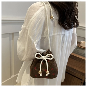 Close-up of brown corduroy bucket bag featuring red strawberry prints and white drawstring bow