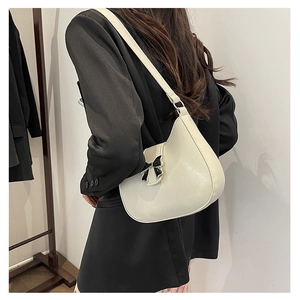 Detail showing cream leather texture and black bow ornament on this shoulder bag