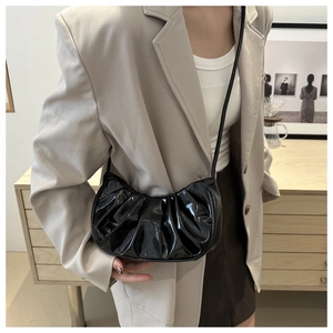 Sac à main croissant en cuir verni noir plissé porté par un mannequin en gros plan