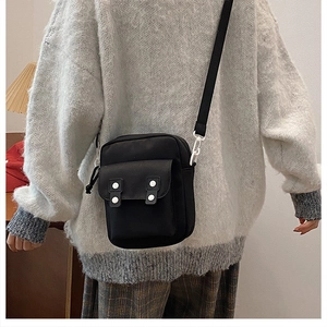 Back view of a mini black canvas messenger bag worn with a casual gray sweater