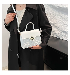Close-up of white quilted handbag featuring a black-gold clover clasp and top handle