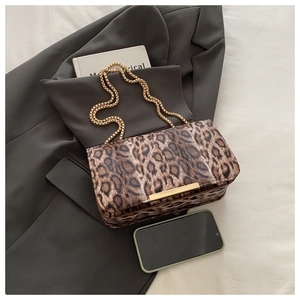 Détail d'un sac à bandoulière léopard avec chaîne dorée et barre en métal sur veste