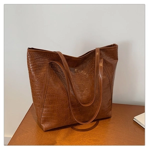 Detail of caramel brown crocodile embossed tote bag with dual shoulder straps on table