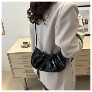 Détail du sac croissant en cuir verni plissé noir porté à l'épaule par un mannequin