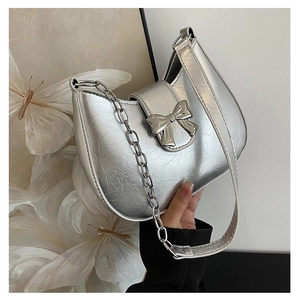 Close-up of a silver metallic crescent bag with a decorative bow and chain strap