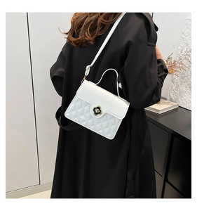 Detail of white quilted crossbody bag with floral gold clasp on black trench coat