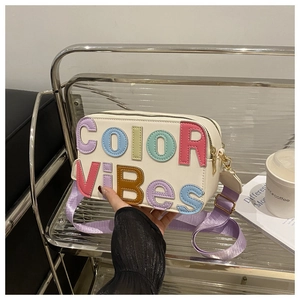 Dettaglio della borsa a tracolla in pelle bianca con lettere COLOR VIBES e tracolla viola